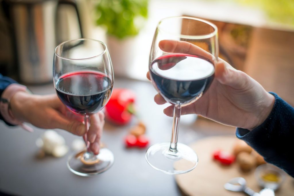 image of two different hands clinking full wine glasses
